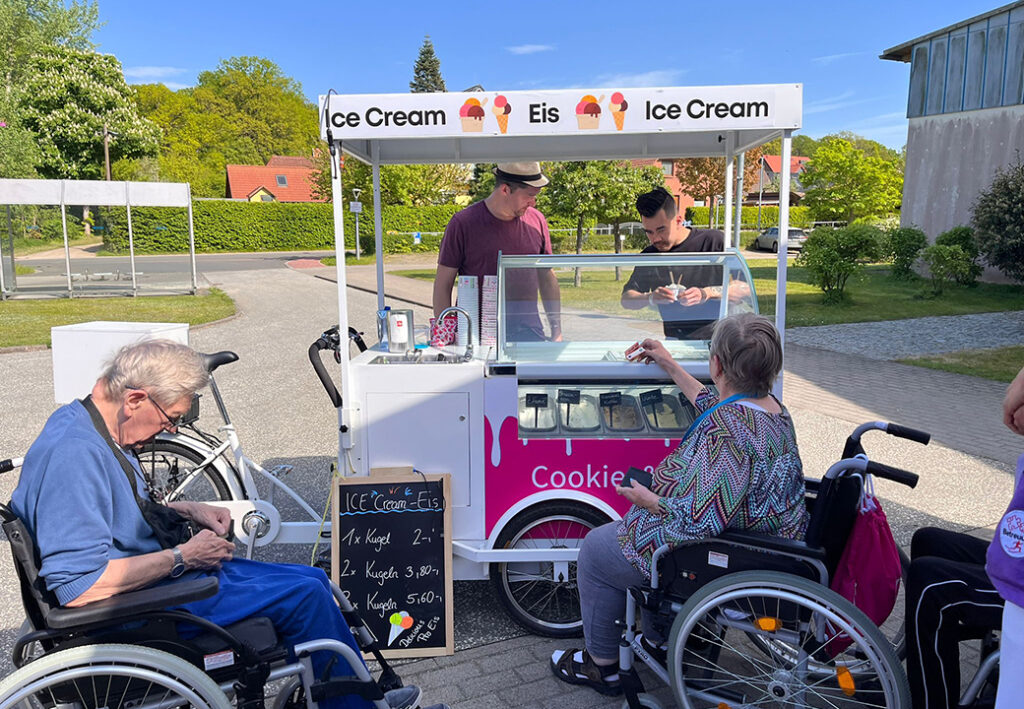 Ein Eiswagen im Freien, umgeben von Menschen in Rollst&uuml;hlen.