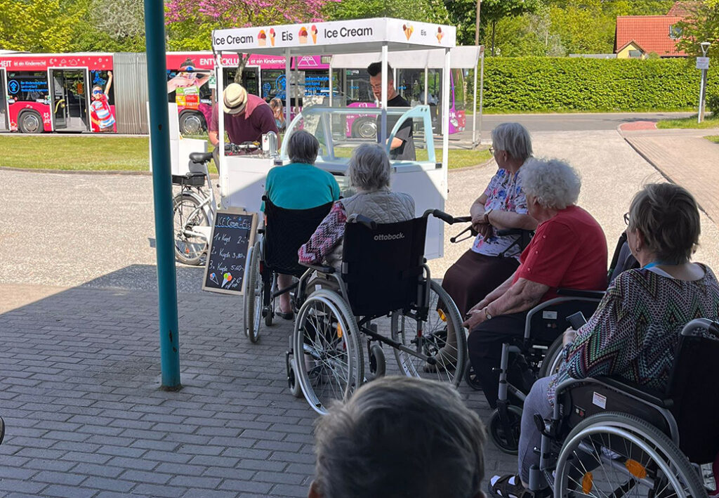 Eine Gruppe &auml;lterer Menschen in Rollst&uuml;hlen wartet vor einem mobilen Eiswagen.