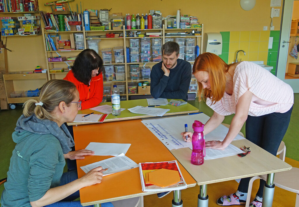 Vier Personen in einem Raum bei einer Besprechung um einen Tisch mit Papieren.