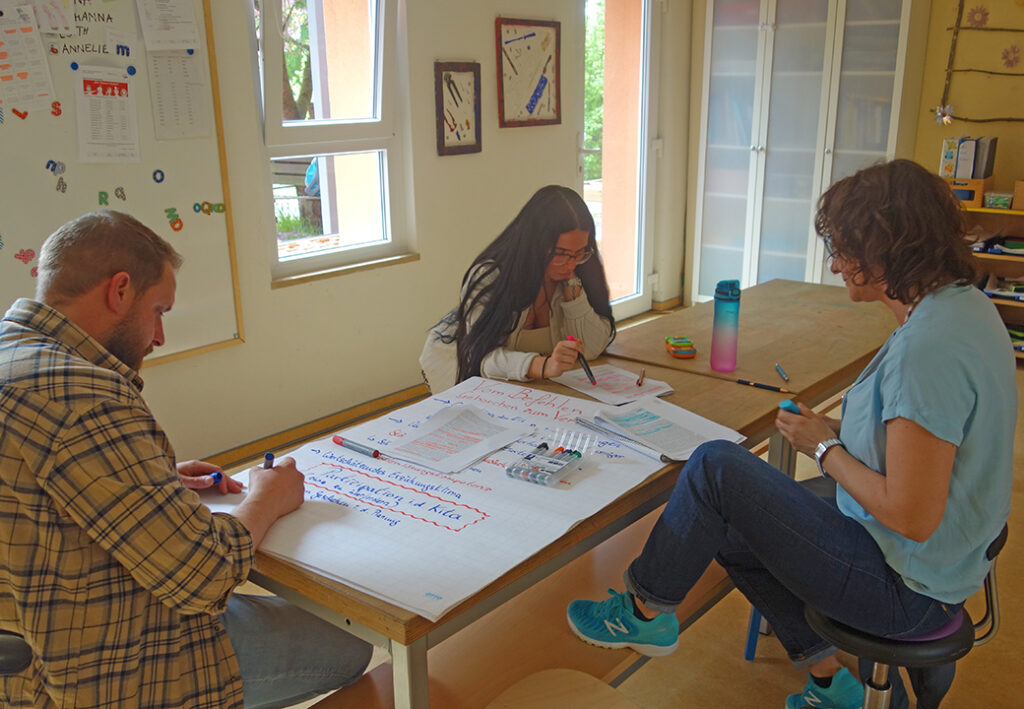 Drei Personen sitzen an einem Tisch und arbeiten an einem Projekt.