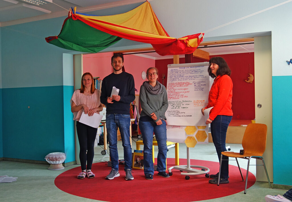 Vier Menschen pr&auml;sentieren vor einem Flipchart in einem bunt dekorierten Raum.
