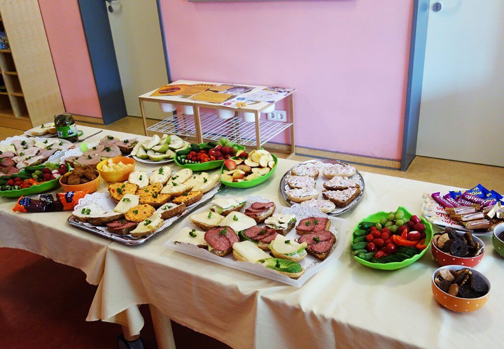 Ein Tisch mit verschiedenen Speisen, darunter belegte Brote, Obst und Snacks.