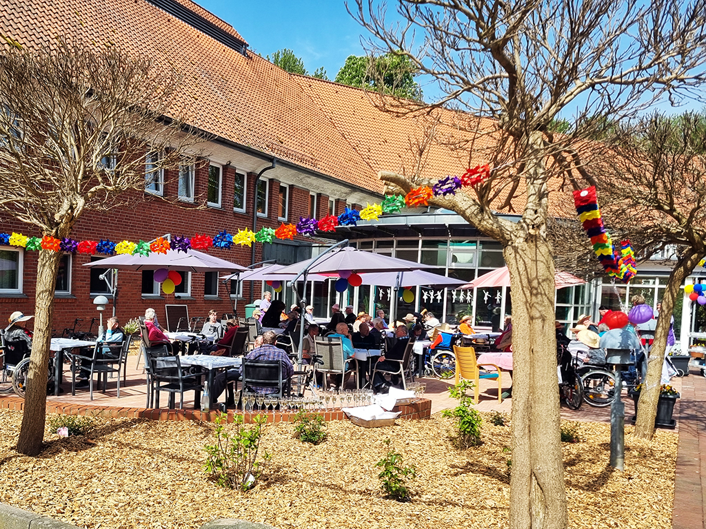 Ein Bild von einer Außenterrasse mit Menschen bei einer Feier unter bunten Girlanden.