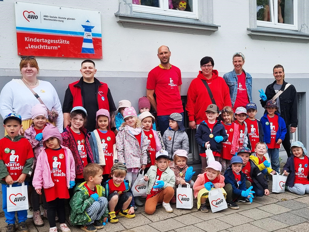 Gruppenfoto von Kindern und Erwachsenen vor der Kindertagesstätte Leuchtturm der AWO-Soziale Dienste gGmbH-Westmecklenburg.