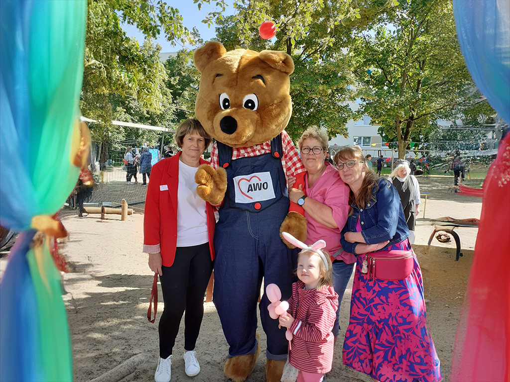 Menschen posieren mit einem Bärenmaskottchen im Freien