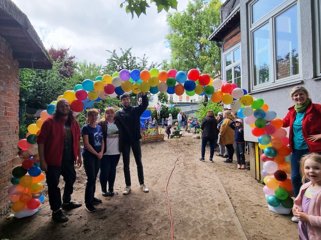 Menschen unter einem Bogen aus bunten Luftballons bei einer Veranstaltung im Freien.