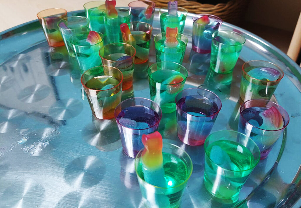 Mehrere Plastikbecher mit buntem Gelee auf einem Tablett.