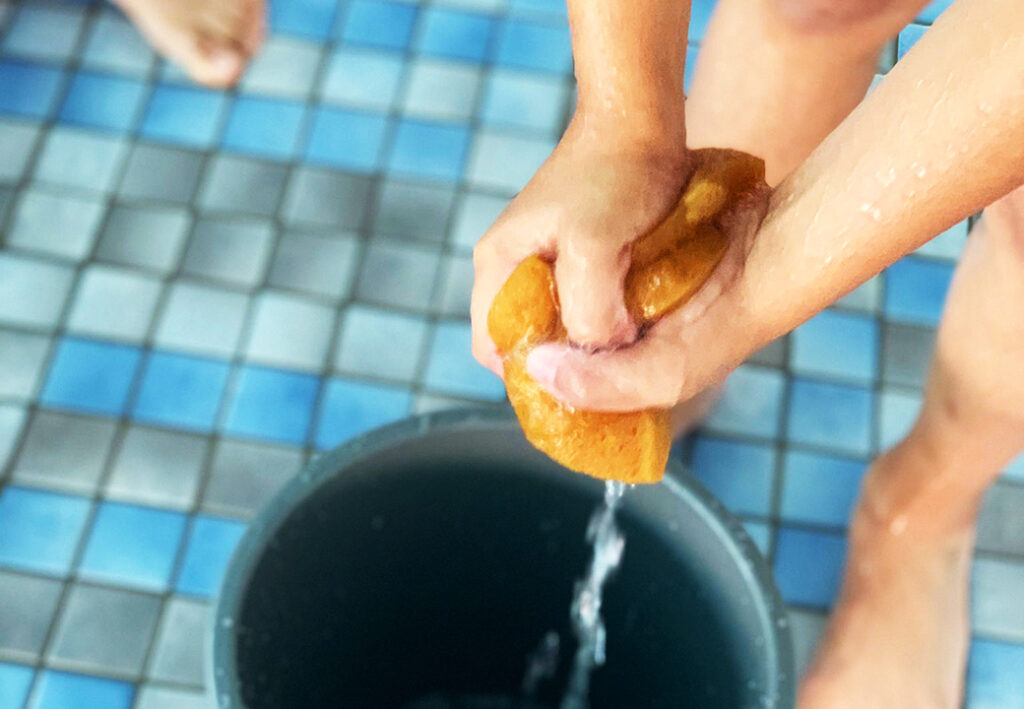 Ein Paar H&auml;nde wringt einen nassen Schwamm &uuml;ber einem Eimer aus.