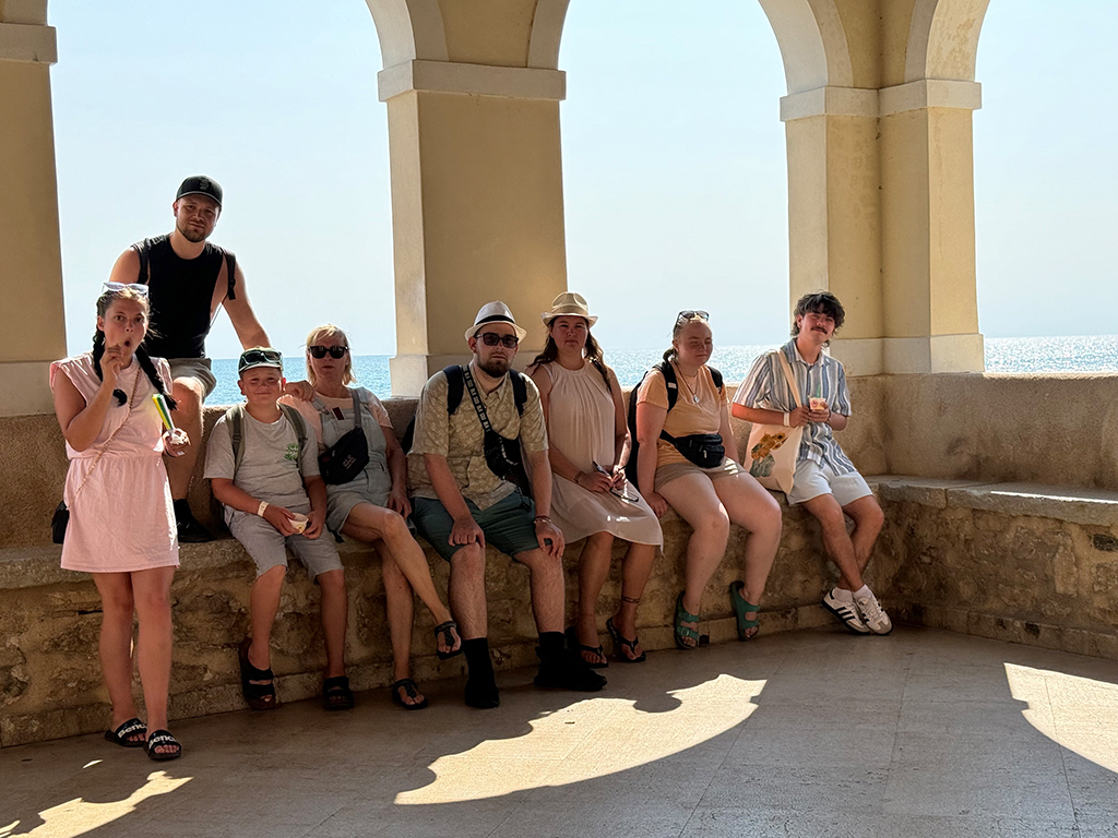 Gruppe von acht Personen sitzt und steht unter einem Bogen am Meer.