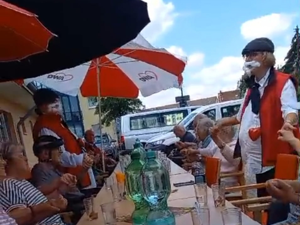 Menschen sitzen an einem gedeckten Tisch im Freien unter AWO-Sonnenschirmen.