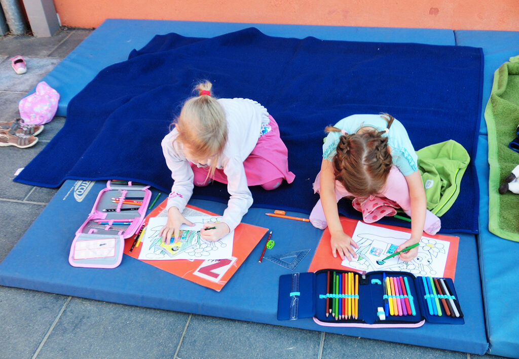 Zwei Mädchen malen auf Matten sitzend.