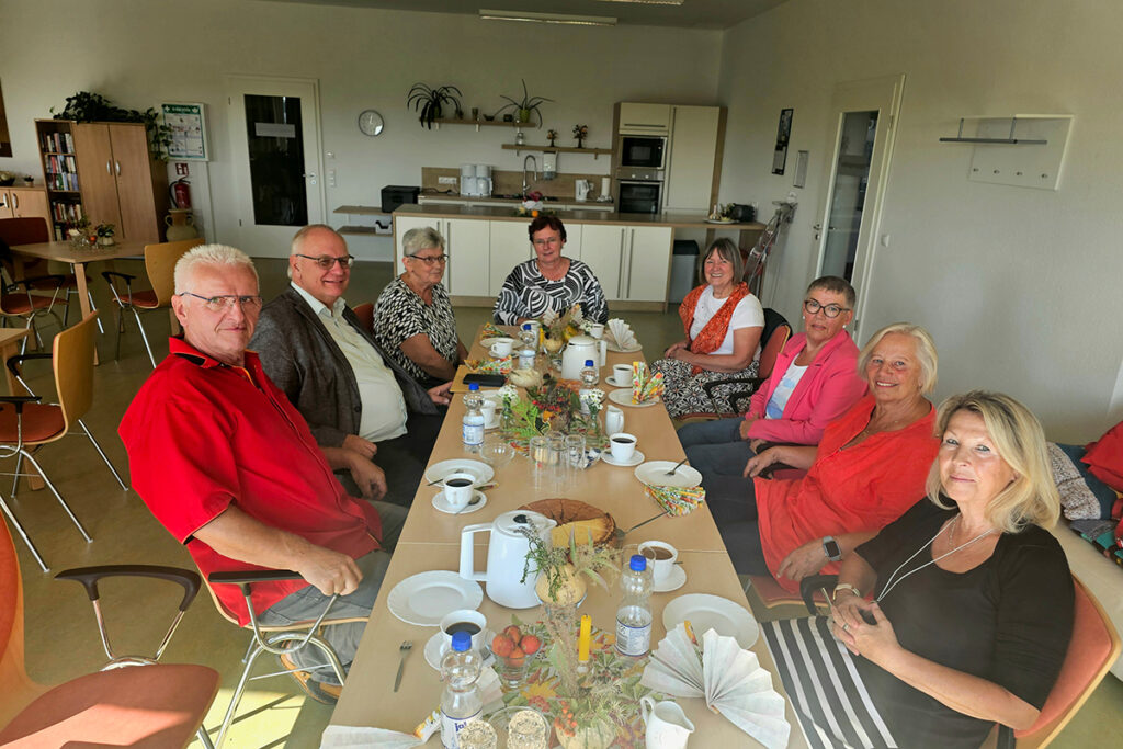Gruppe von Menschen sitzt um einen gedeckten Tisch in einem Gemeinschaftsraum.