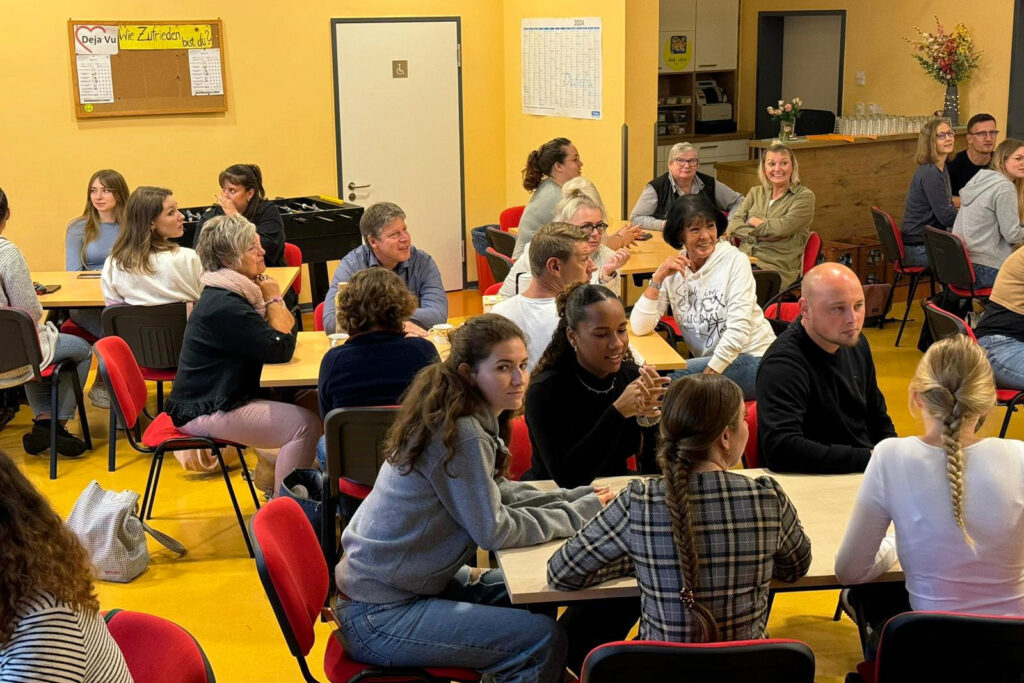 Menschen sitzen in einem Raum an Tischen und unterhalten sich.