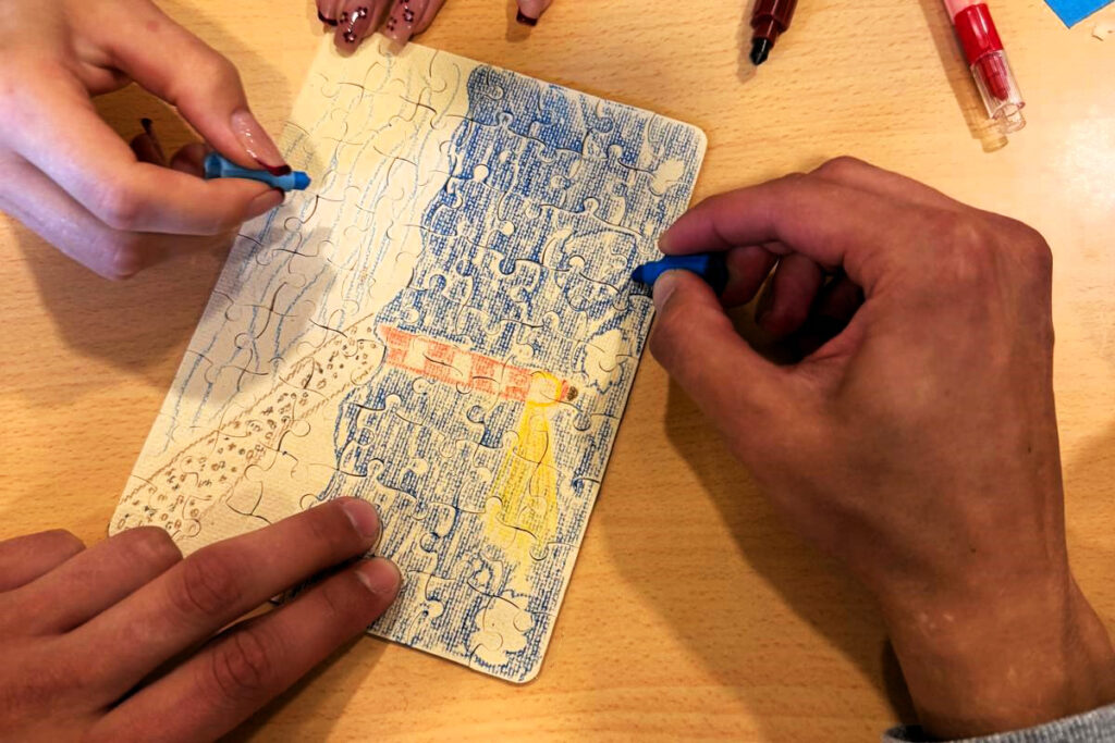 Zwei Personen malen ein Puzzle an einem Tisch aus.