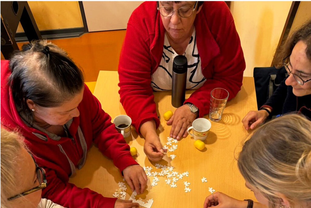 F&uuml;nf Personen puzzeln gemeinsam an einem Tisch.