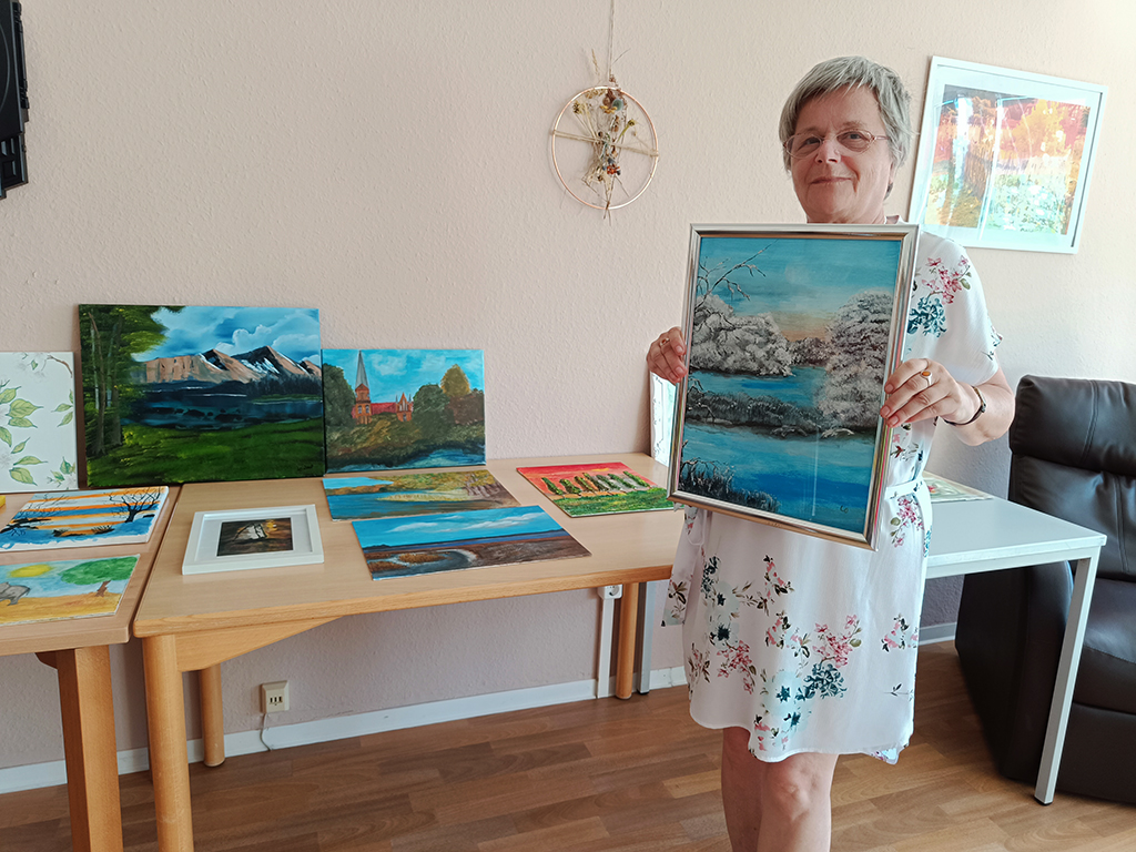 Frau hält ein Gemälde in einem Raum voller Kunstwerke.