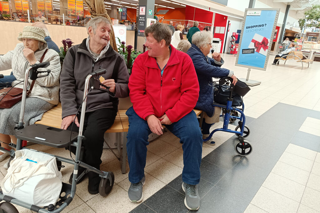 Gruppe von &auml;lteren Menschen sitzt auf einer Bank in einem Einkaufszentrum.
