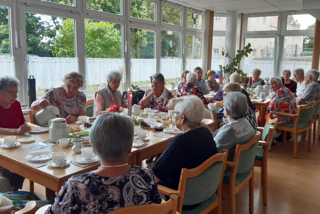 Gruppen von Senioren beim Kaffeetrinken in einem hellen Raum.