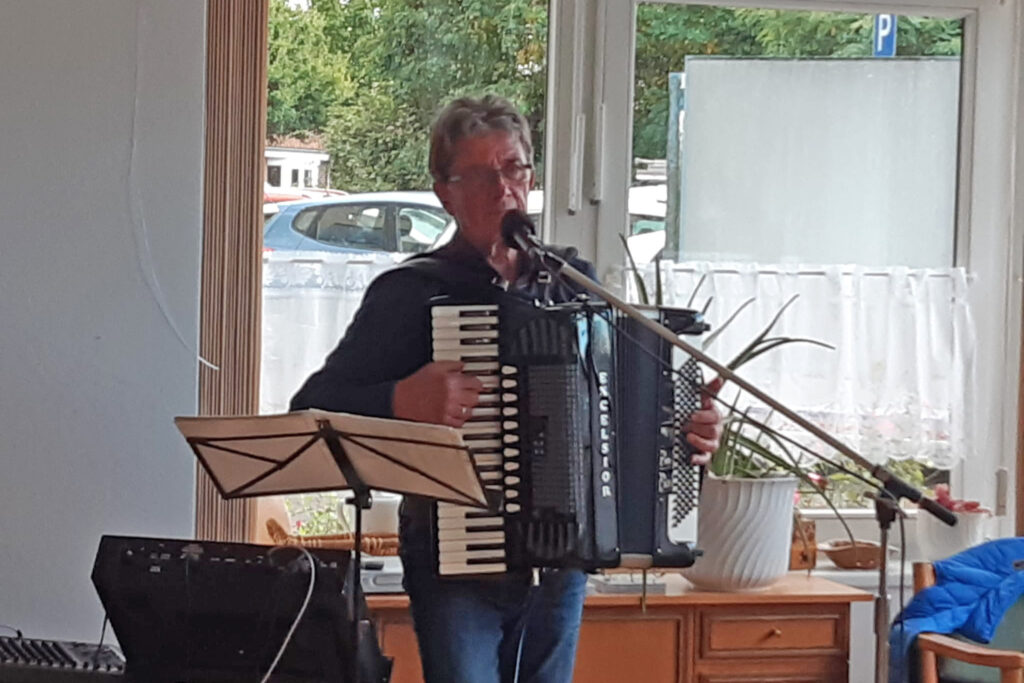 Mann spielt Akkordeon und singt in einem Raum mit gro&szlig;en Fenstern