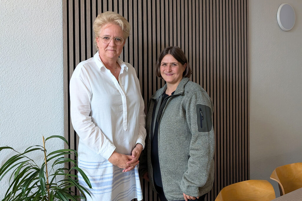 Zwei Personen stehen in einem Raum nebeneinander.