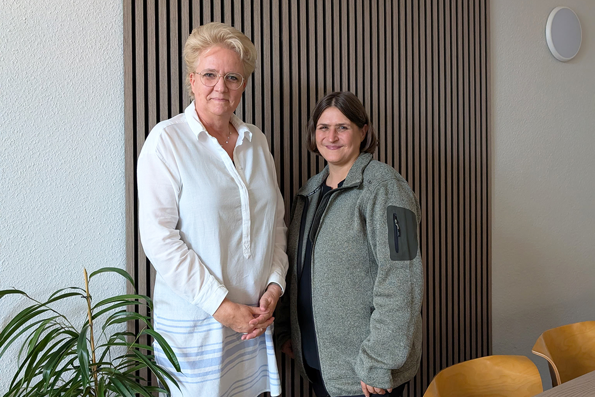 Zwei Personen stehen in einem Raum nebeneinander.