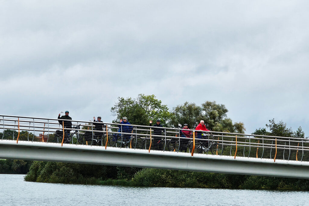 Menschen auf einer Br&uuml;cke mit Fahrr&auml;dern bei bew&ouml;lktem Himmel.