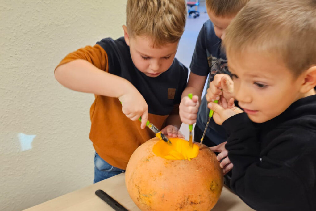 Drei Kinder schnitzen an einem K&uuml;rbis.