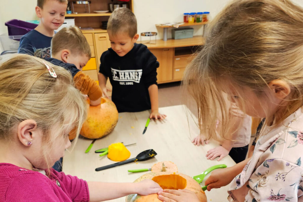 Kinder schnitzen K&uuml;rbisse in einem Raum.