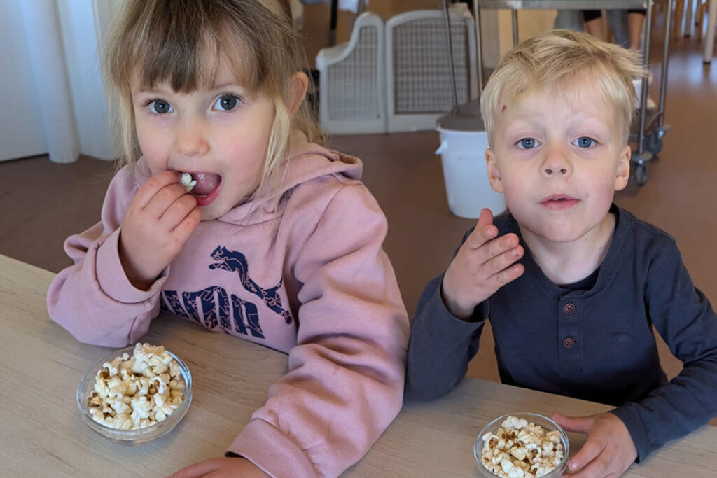 Zwei Kinder sitzen an einem Tisch und essen Popcorn.