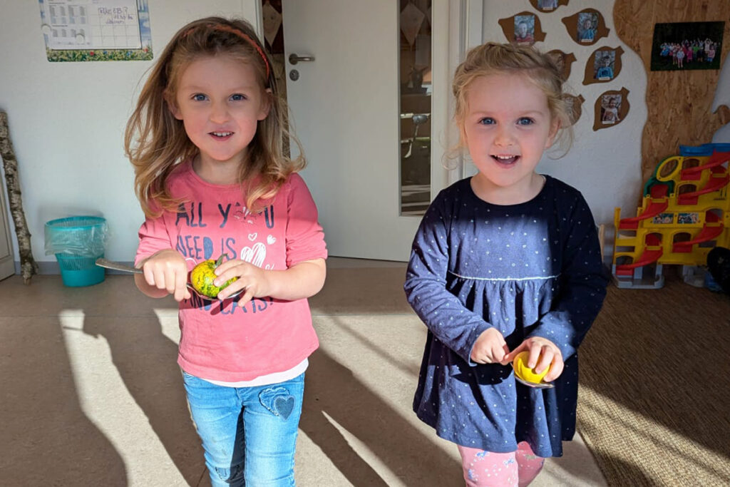 Zwei kleine Kinder stehen nebeneinander und halten Spielzeug in den H&auml;nden.