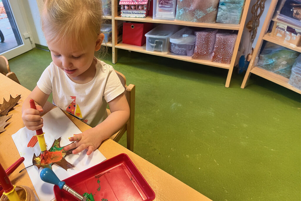 Kind bei einer Bastelaktivit&auml;t mit einem Herbstblatt.