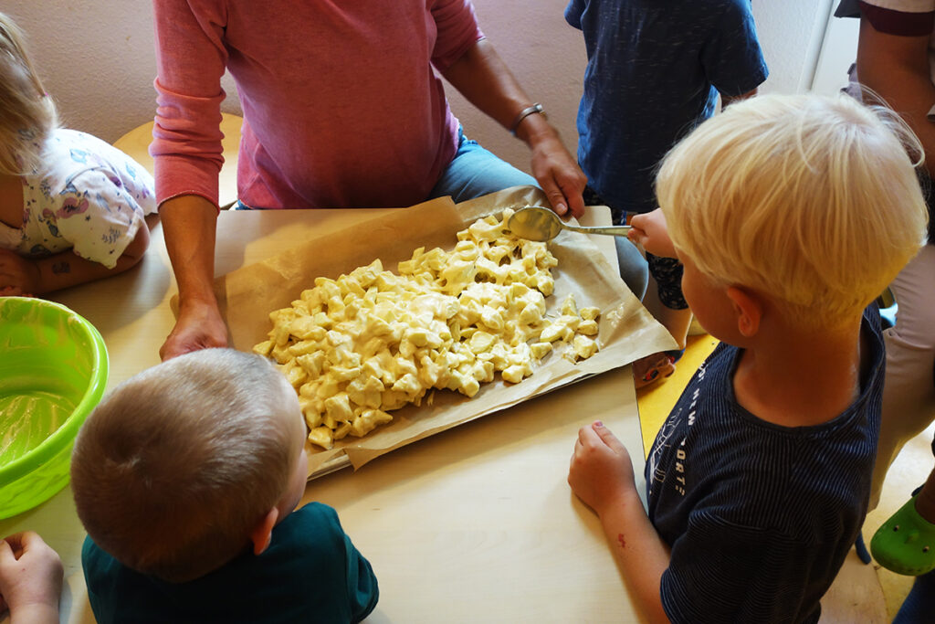 Kinder bereiten ein Backblech mit Nudeln vor