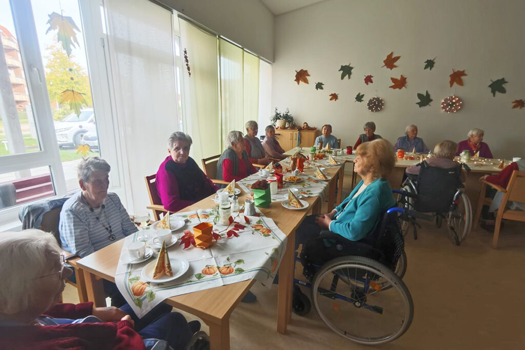 &Auml;ltere Menschen sitzen in einem Gemeinschaftsraum an einem gedeckten Tisch.