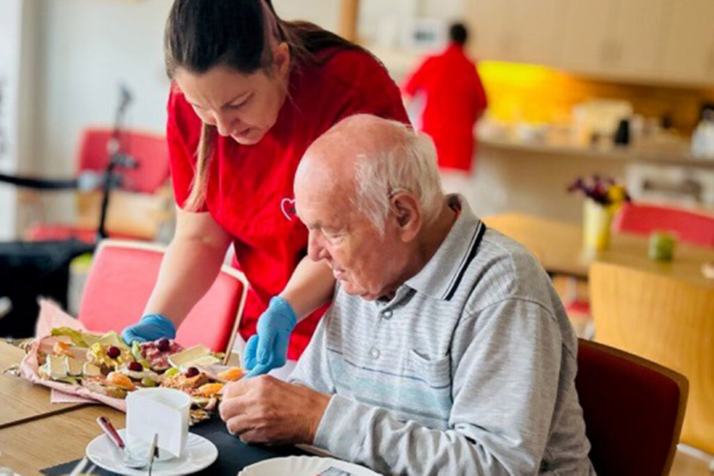 Eine Pflegekraft hilft einem &auml;lteren Mann beim Essen.