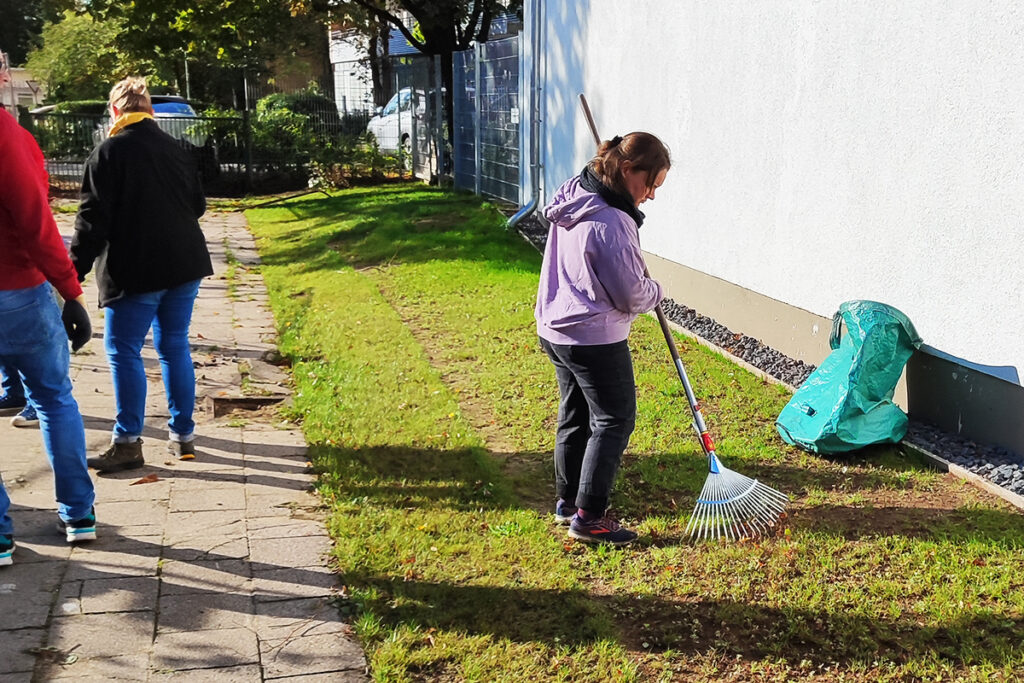 Personen bei der Gartenarbeit, sammeln Laub mit Rechen.