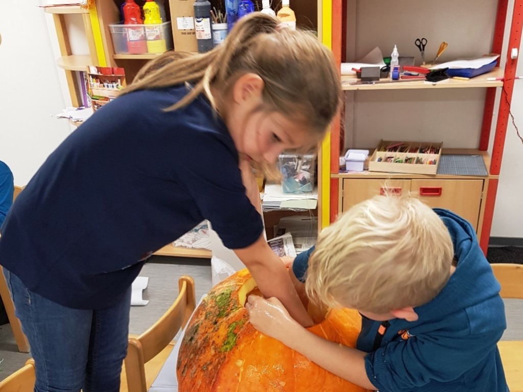Zwei Kinder beschäftigen sich mit einem großen Kürbis in einem Bastelraum