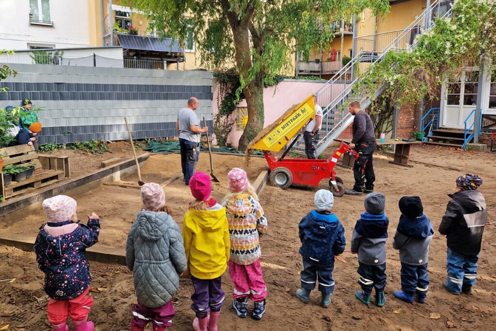 Kinder schauen zu, wie Erwachsene einen Sandbereich vorbereiten
