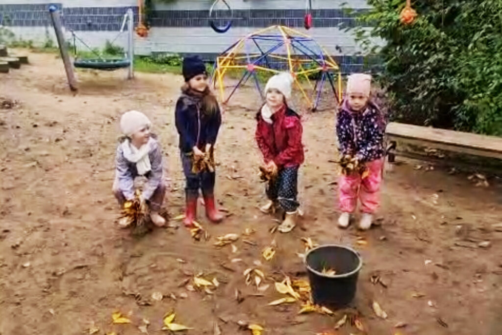 Vier Kinder auf einem Spielplatz sammeln Herbstbl&auml;tter.