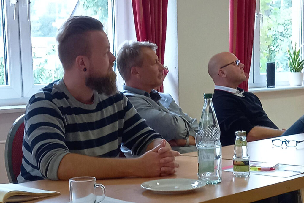 Drei M&auml;nner sitzen am Tisch in einem Meeting.