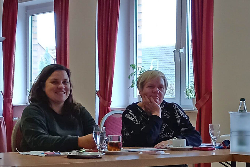 Zwei Frauen sitzen an einem Tisch und l&auml;cheln.