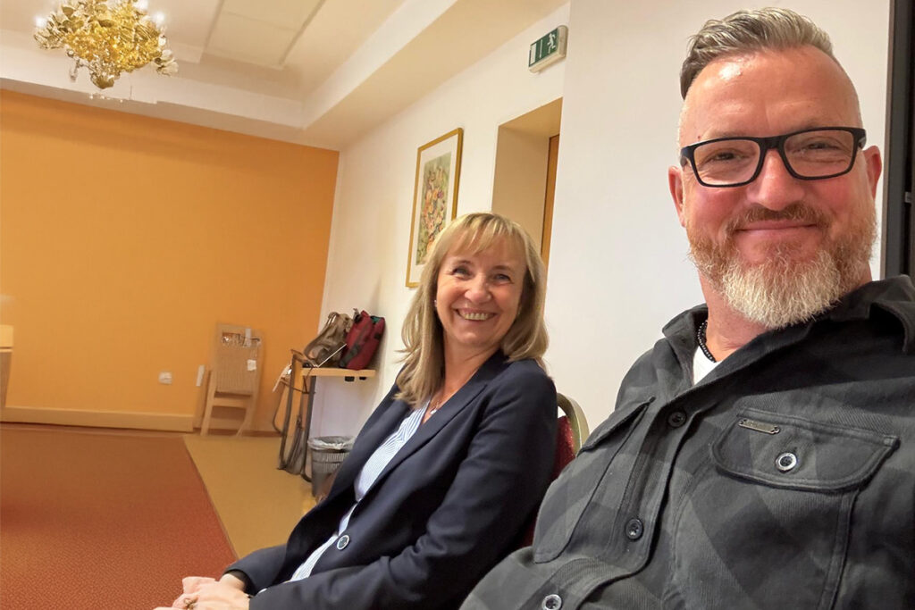 Zwei Personen sitzen l&auml;chelnd in einem Raum.