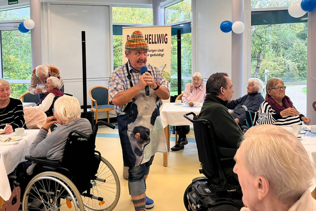 Eine gesellige Veranstaltung in einem Gemeinschaftsraum mit Senioren und einem unterhaltenden Moderator.