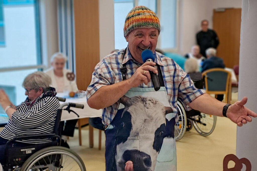 Mann mit Mikrofon f&uuml;hrt vor &auml;lteren Menschen eine Unterhaltung auf.