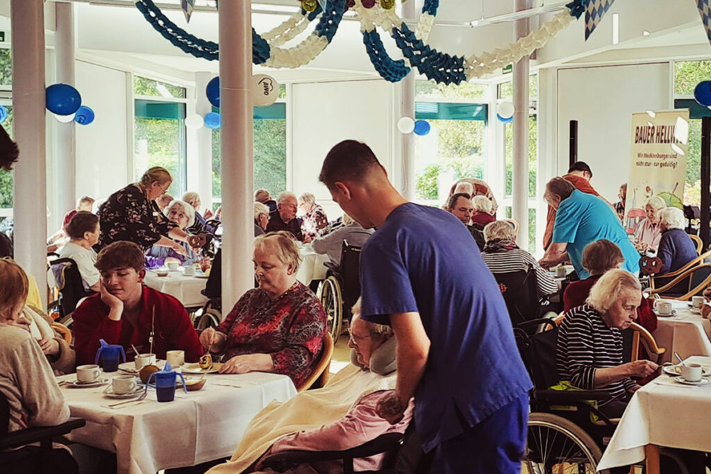 Menschen in einem festlich geschm&uuml;ckten Raum sitzen an Tischen und unterhalten sich.