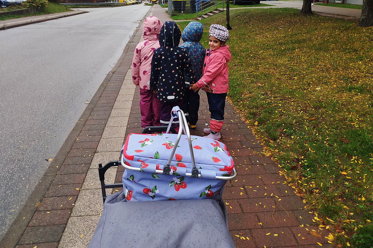 Gruppe von fünf Kindern in wetterfester Kleidung, die auf einem Gehweg spazieren gehen.