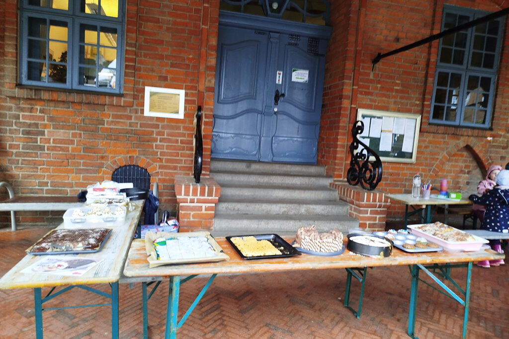 Ein Bild von einer Backsteinfassade mit Holztischen vor der Eingangst&uuml;r.