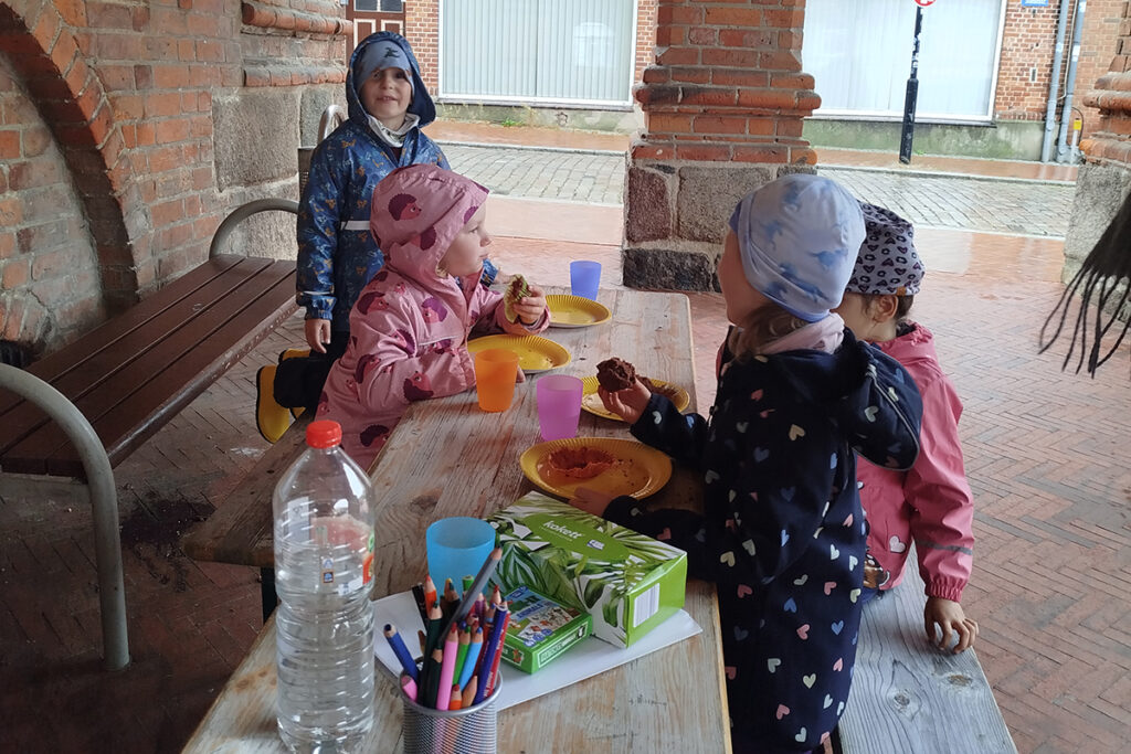 Mehrere Kinder sitzen an einem Holztisch und essen Muffins