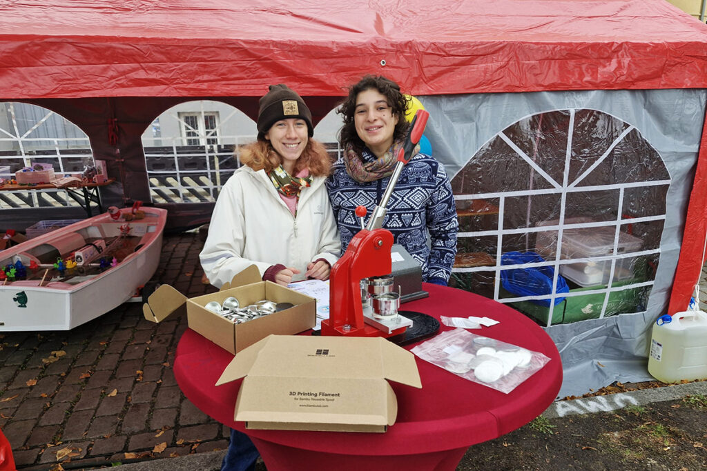 Zwei Personen an einem Tisch mit einer Buttonmaschine