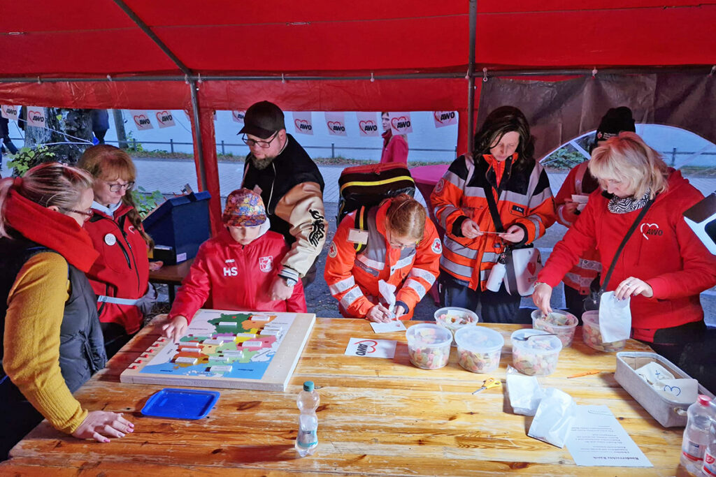 Gruppe von Menschen in roter und schwarzer Kleidung versammelt um einen Tisch in einem Zelt.