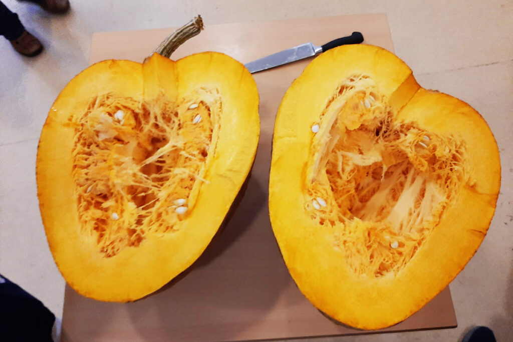 Zwei Hälften eines aufgeschnittenen Kürbisses auf einem Tisch mit einem Messer daneben